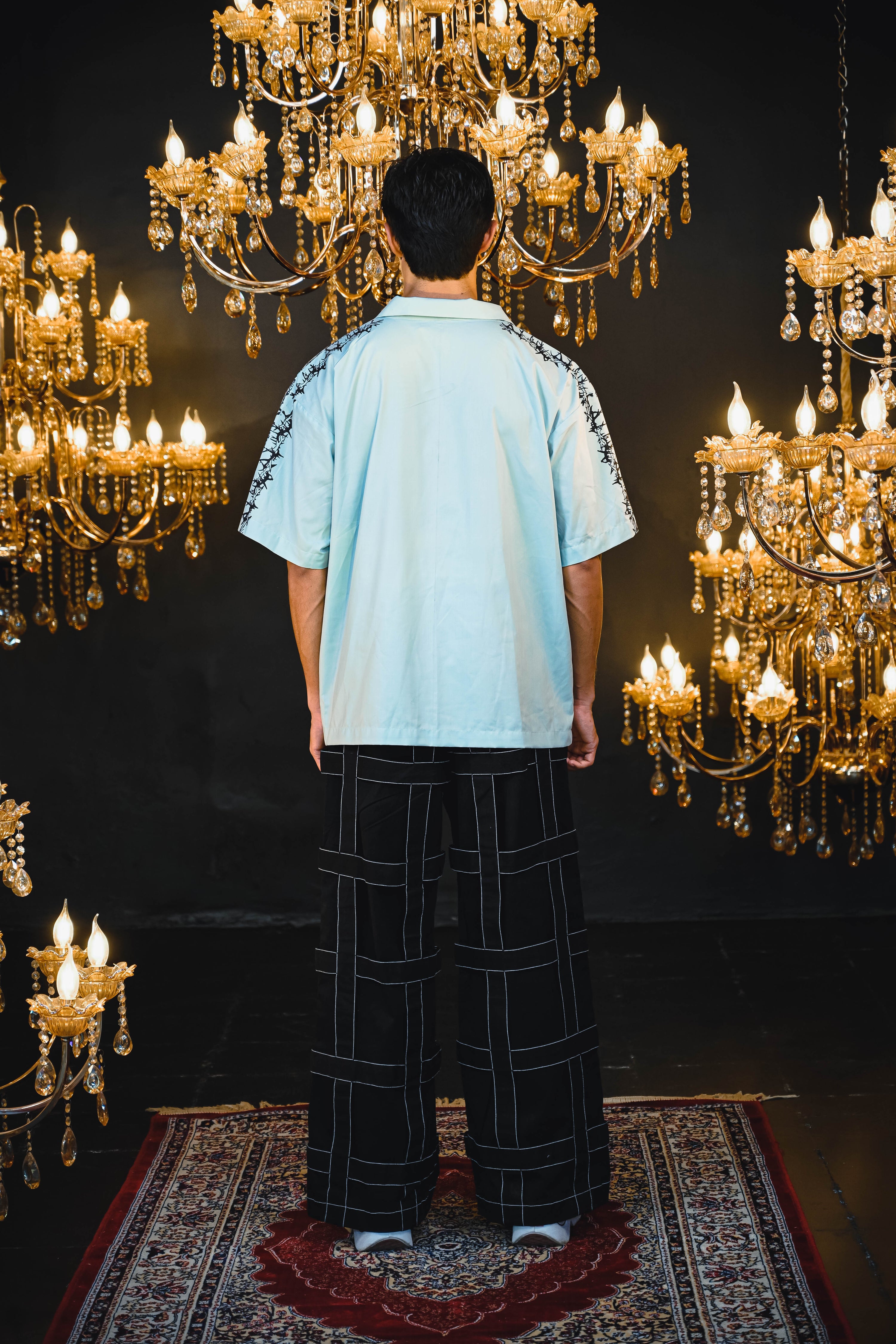 Person wearing a light blue shirt with white patterns in a room with chandeliers.